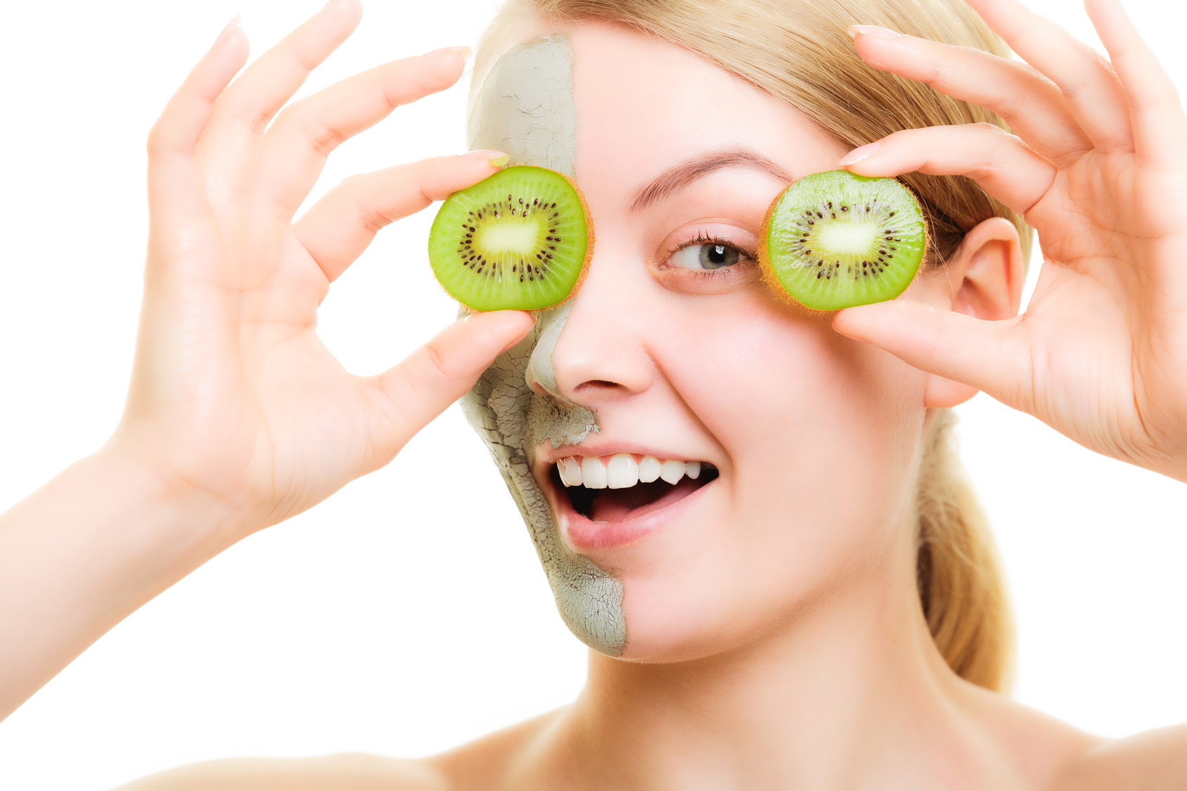 Skin care. Woman in clay mud mask on face holding slices of kiwi fruit isolated. Girl taking care of dry complexion.